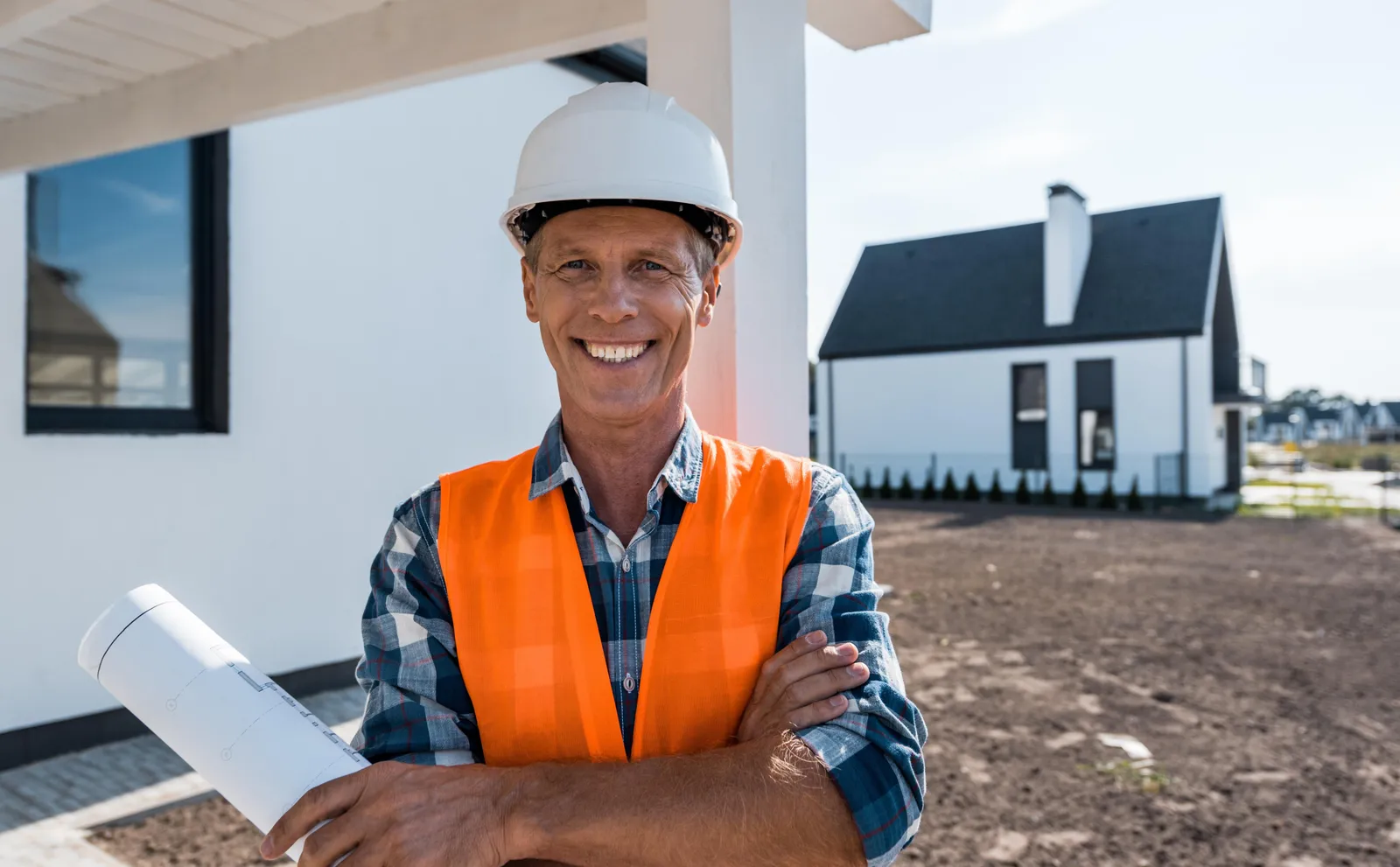 Tradesperson holding blueprints outside a new home